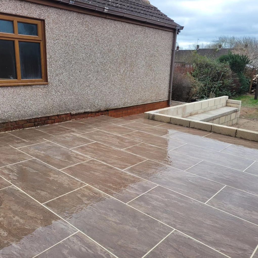 Warm-toned paving patio beside a pebble-dashed house with new block retaining walls