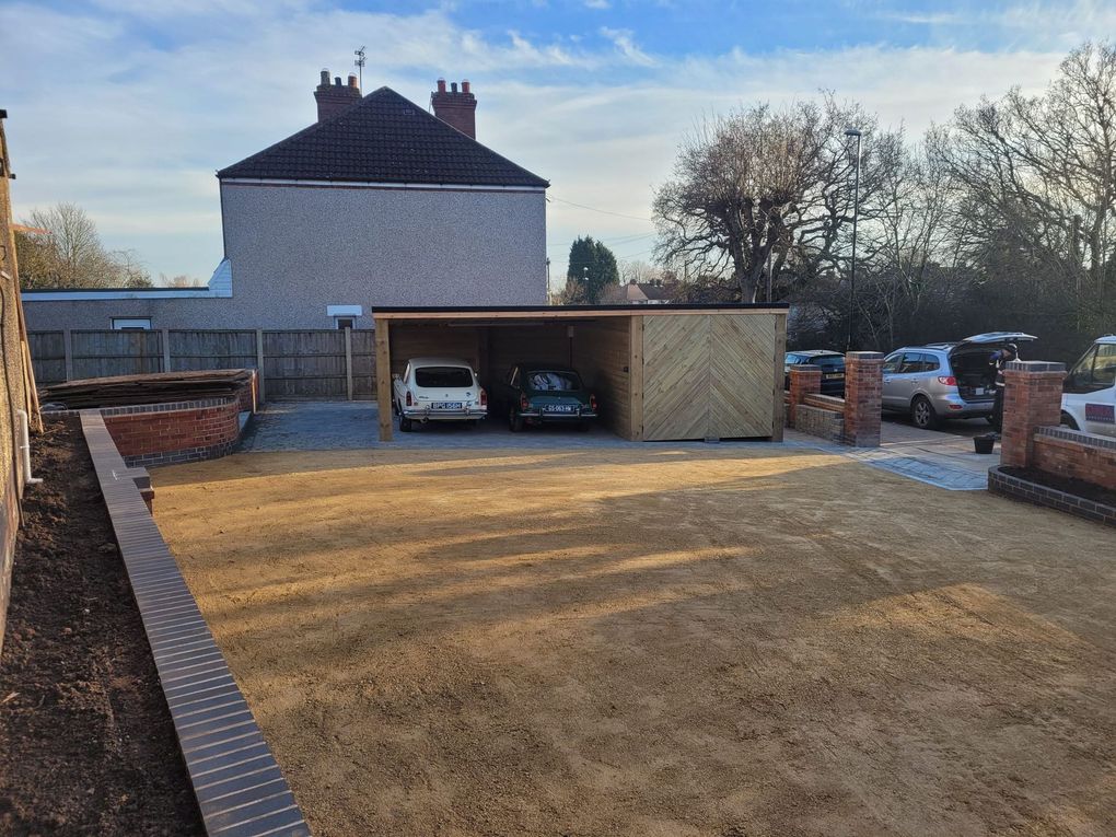 Wide compacted gravel frontage with brick-edged beds and walls and a timber carport at the far end