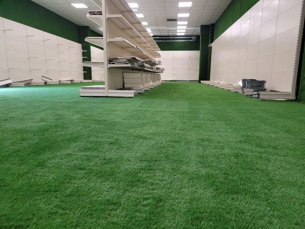 Artificial grass covering the floor of an indoor showroom between rows of empty shelving
