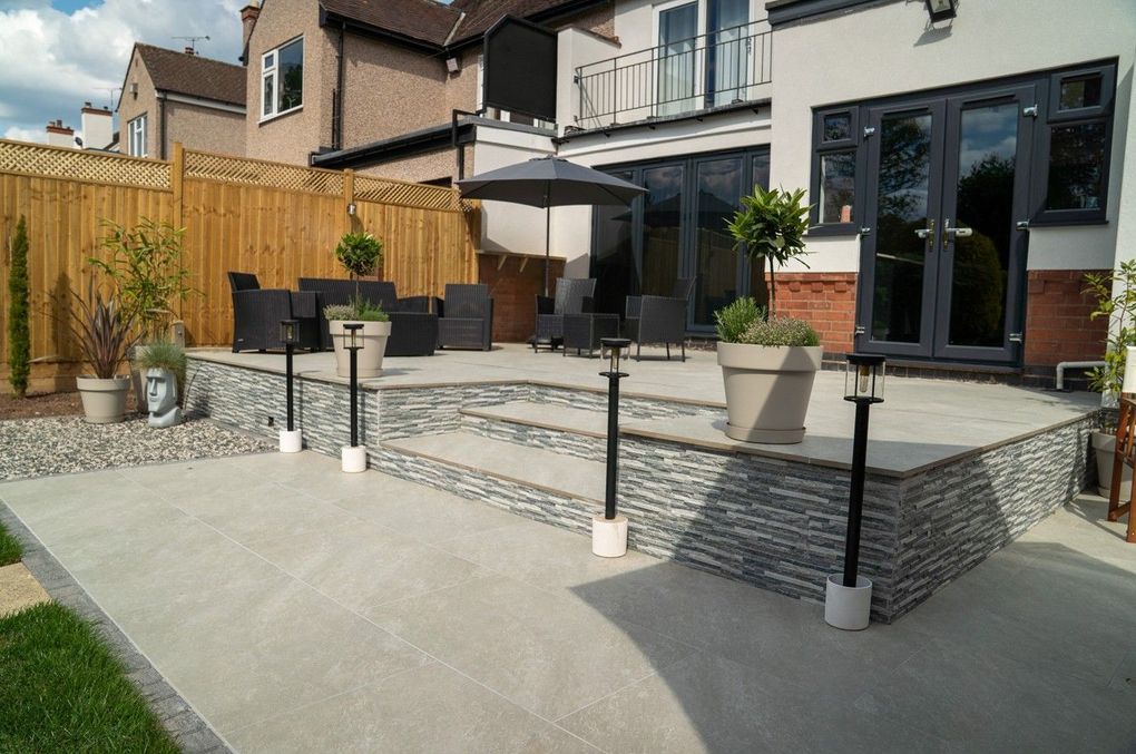 Two-level light grey porcelain terrace with a stone-clad retaining wall and lantern posts in Earlsdon, Coventry