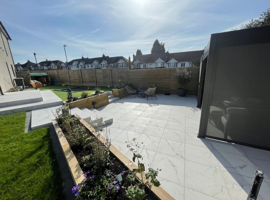 Sleeper-edged raised bed of flowering plants beside the marble-effect porcelain terrace in the Coundon garden