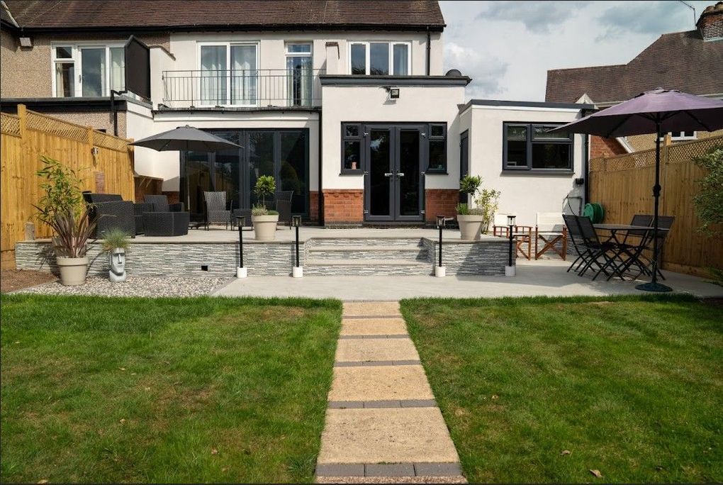The same Earlsdon garden after landscaping, with a two-level light grey porcelain terrace, stone-clad retaining wall and steps lined up with the existing lawn path