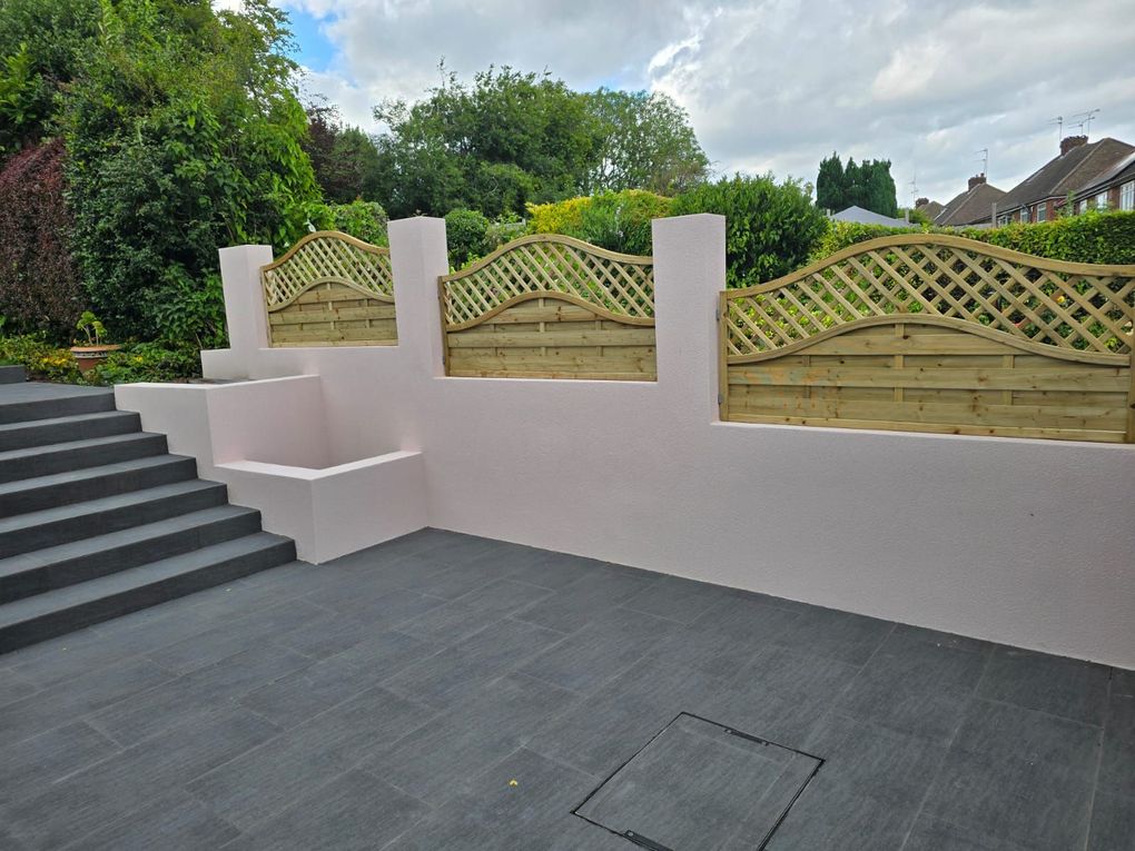 Wide porcelain steps between rendered retaining walls topped with lattice fencing in a tiered garden