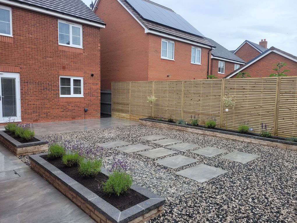 Brick-edged raised beds, gravel and stepping stones behind a new-build house with slatted fencing