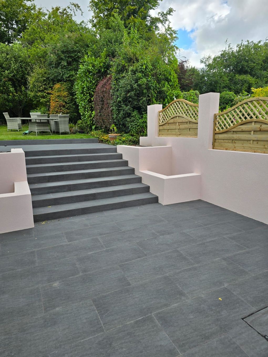 Finished porcelain steps between rendered walls rising to the upper lawn with lattice-topped fencing