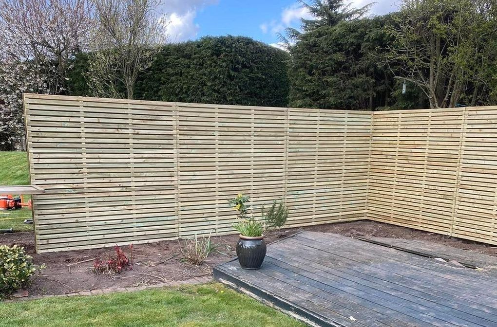 New pressure-treated slatted privacy fencing running round the corner of a garden with a hedge behind