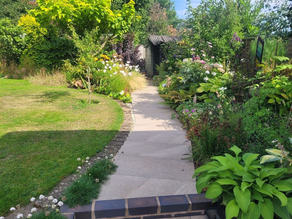 Curved path between a lawn and deep planted borders full of shrubs and perennials