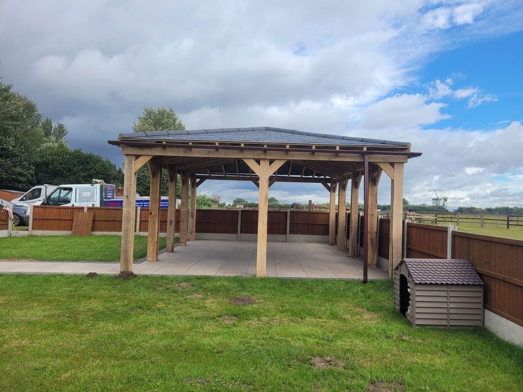 End view of a long timber gazebo with braced posts and a tiled roof over paving