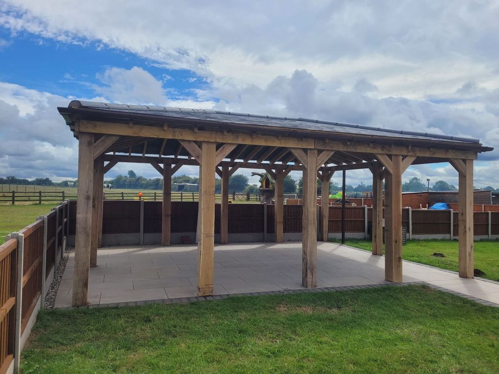 Large timber gazebo with a tiled hipped roof over a paved seating area, with open fields beyond