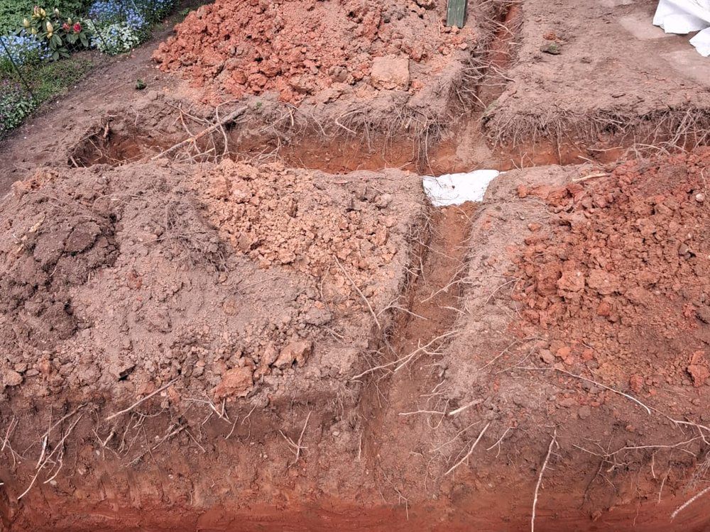 Open drainage trenches cut into dense red clay subsoil in a Warwickshire garden