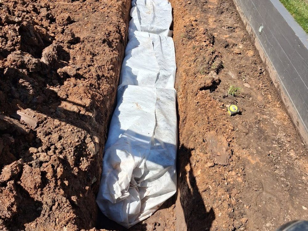 Soakaway crate wrapped in geotextile membrane set into an excavated pit beside a house
