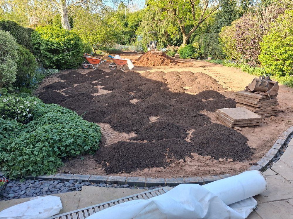 Screened topsoil spread across a drained garden with rolls of turf stacked ready to lay