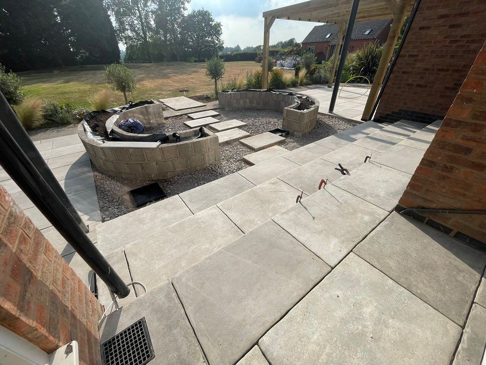 View from the house over new porcelain paving, curved planters and gravel towards the wider garden at Lapworth