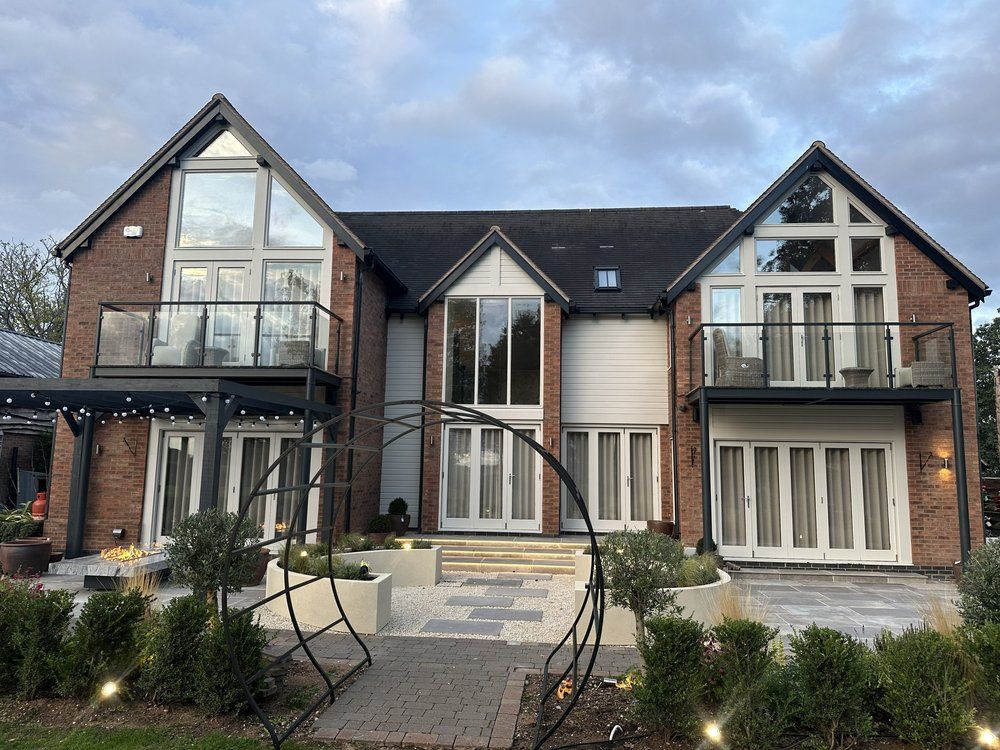 Finished garden at dusk with a circular Moon Gate pergola, rendered planters, porcelain steps and lit house elevation at Chestnut House, Lapworth