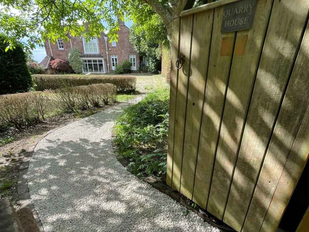 Timber gate with Quarry House name plate and gravel path leading to a Grade II listed sandstone home near Coleshill