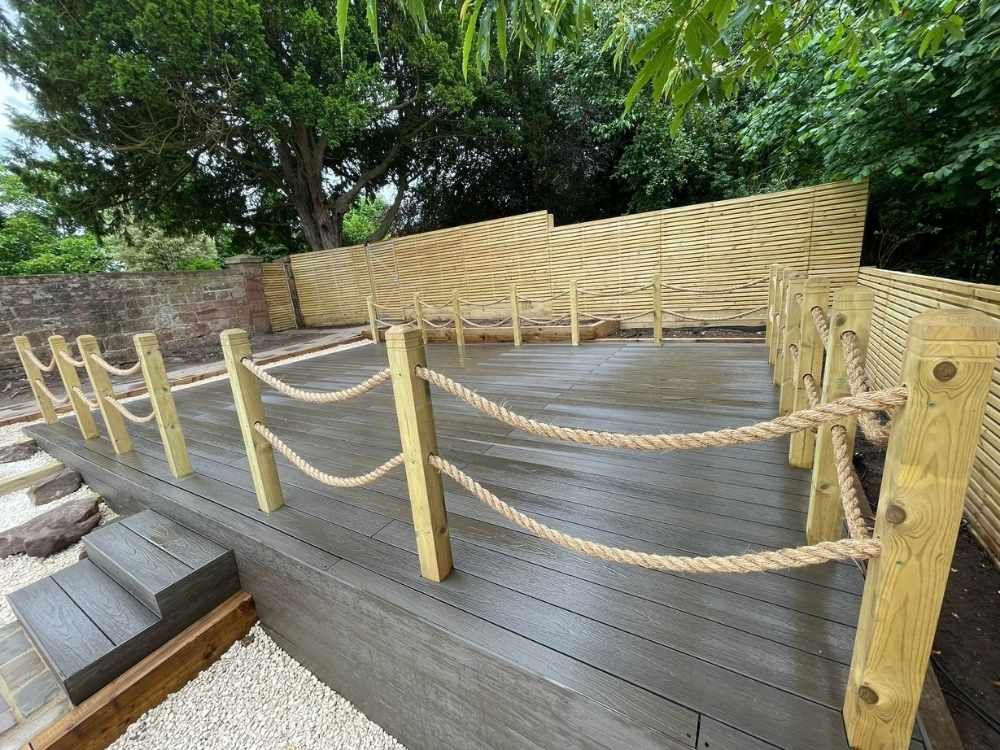 Raised walnut composite decking terrace with rope balustrade between timber posts and slatted fencing behind