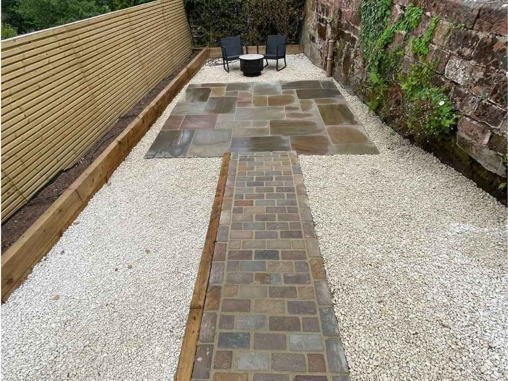 Sandstone paved fire pit area with two chairs, setts path and slatted fencing beside an original mossy sandstone wall