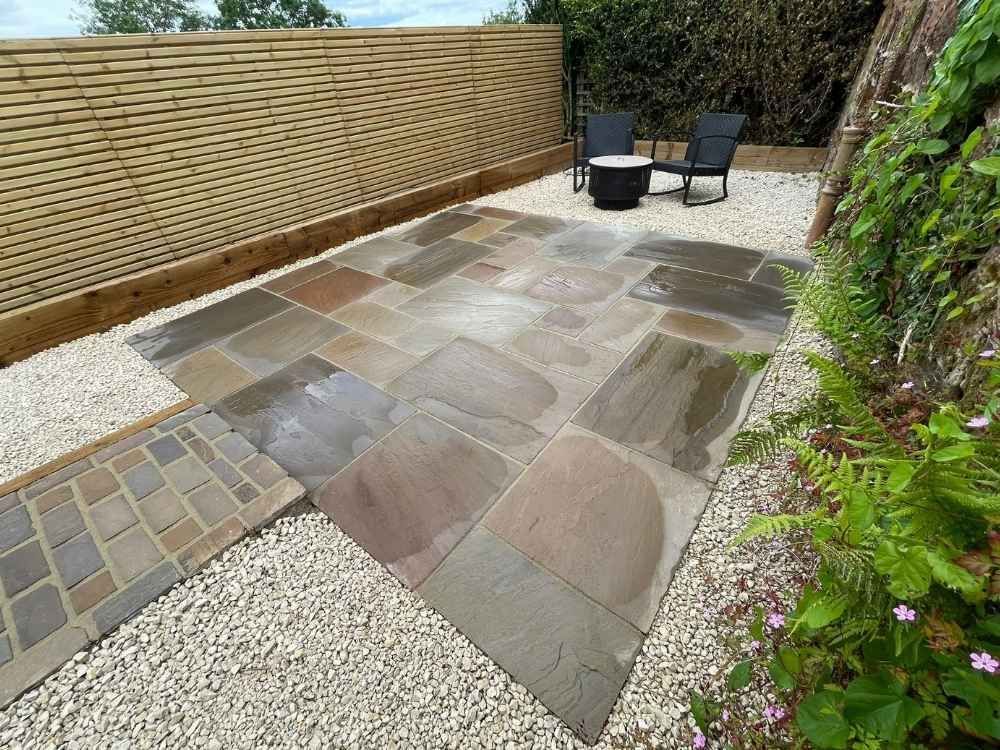Sandstone fire pit terrace with ferns and pink flowering planting establishing against the original stone wall
