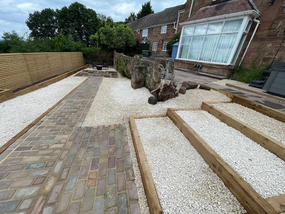 Landscaped garden with white gravel, sandstone setts path, sleeper steps and decorative boulders at Quarry House