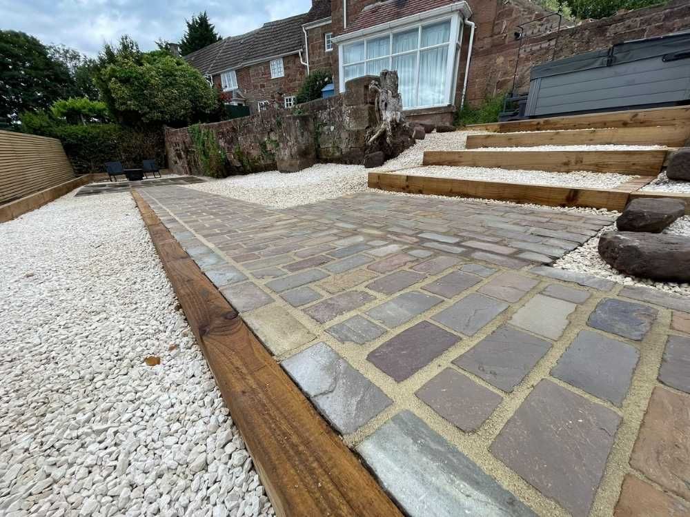 Sandstone setts paving with timber sleeper steps, white gravel and decorative boulders below the listed house