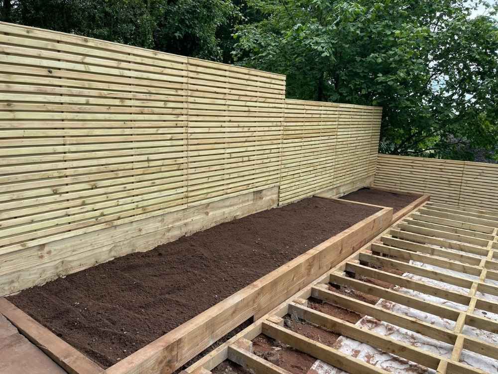 Six-foot contemporary slatted timber fencing with a railway sleeper retaining bed filled with topsoil
