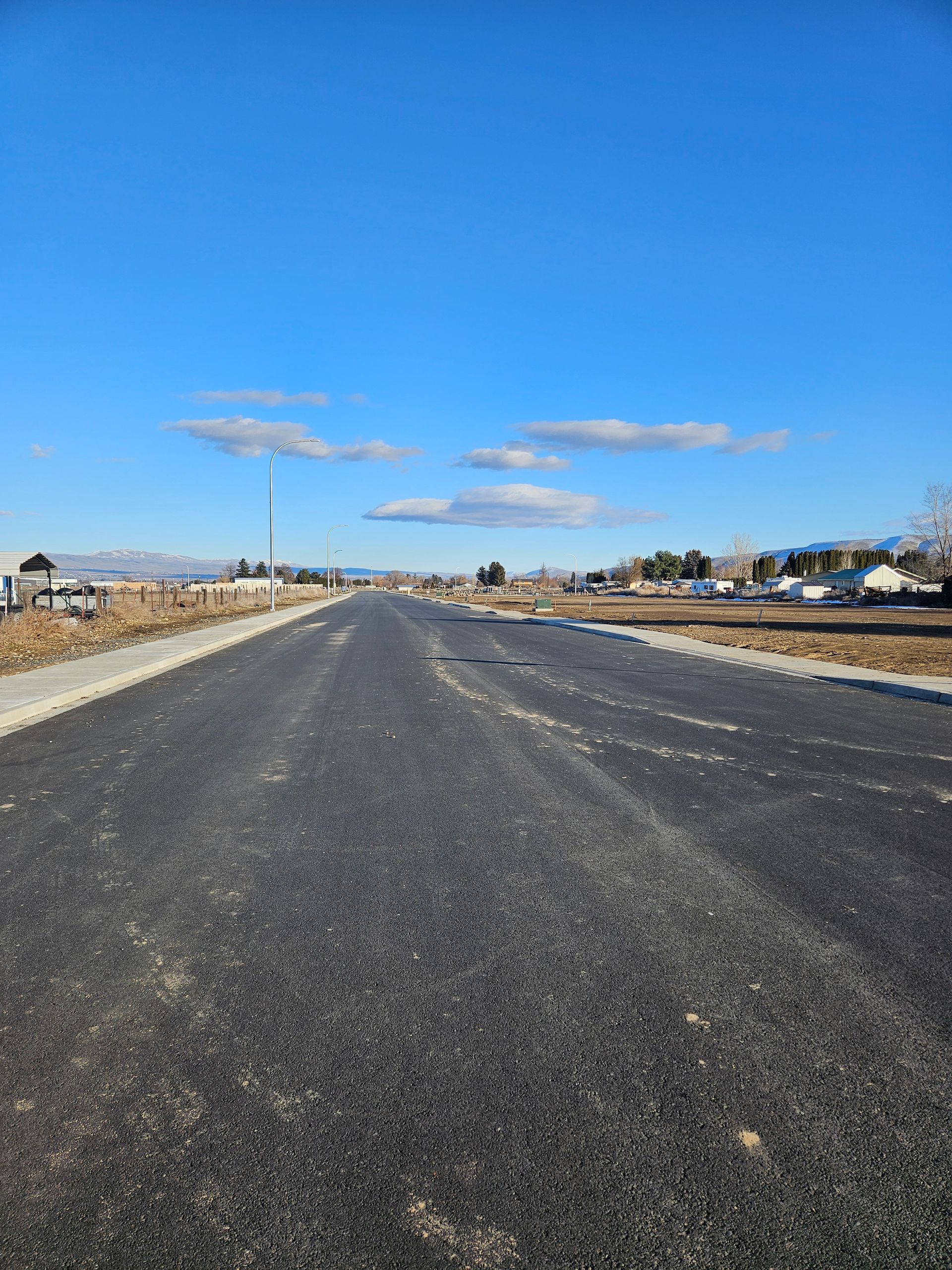 Empty paved road stretching into a rural neighborhood under a clear blue sky.