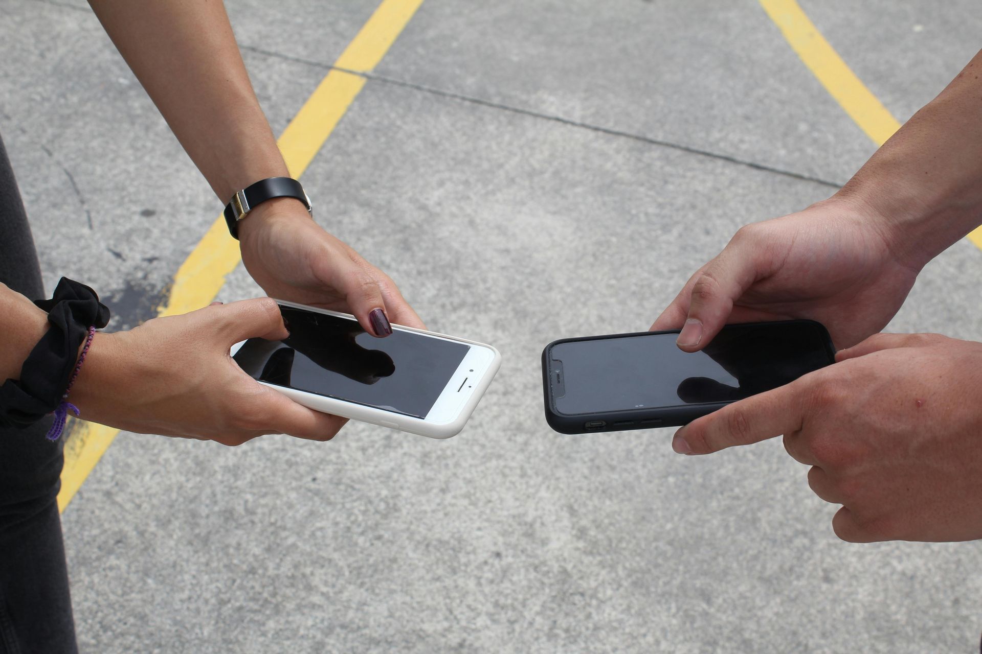Two people holding smartphones together over a concrete surface with yellow lines