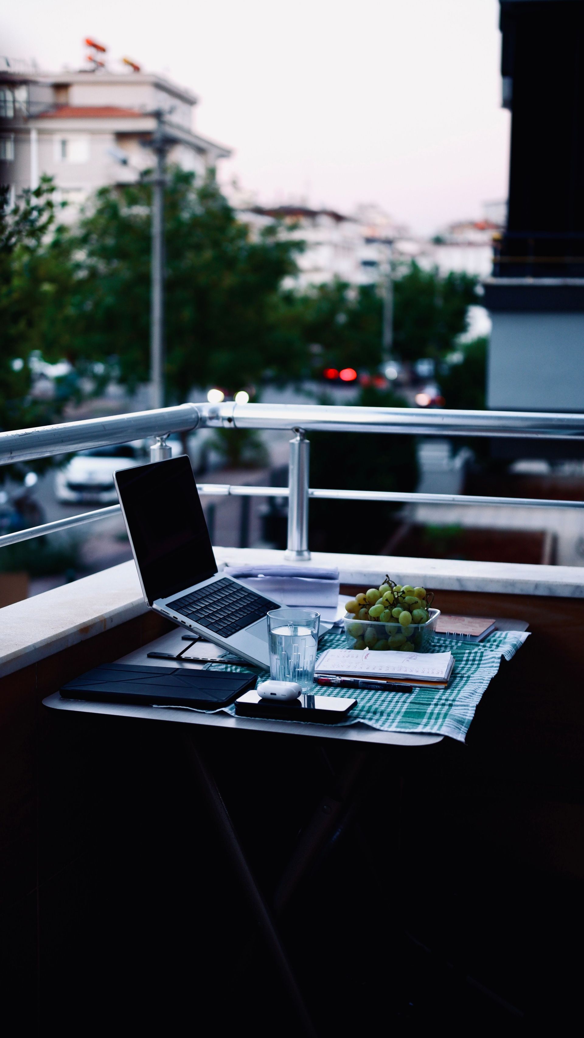 Laptop and coffee on a balcony table overlooking a blurred city street at dusk