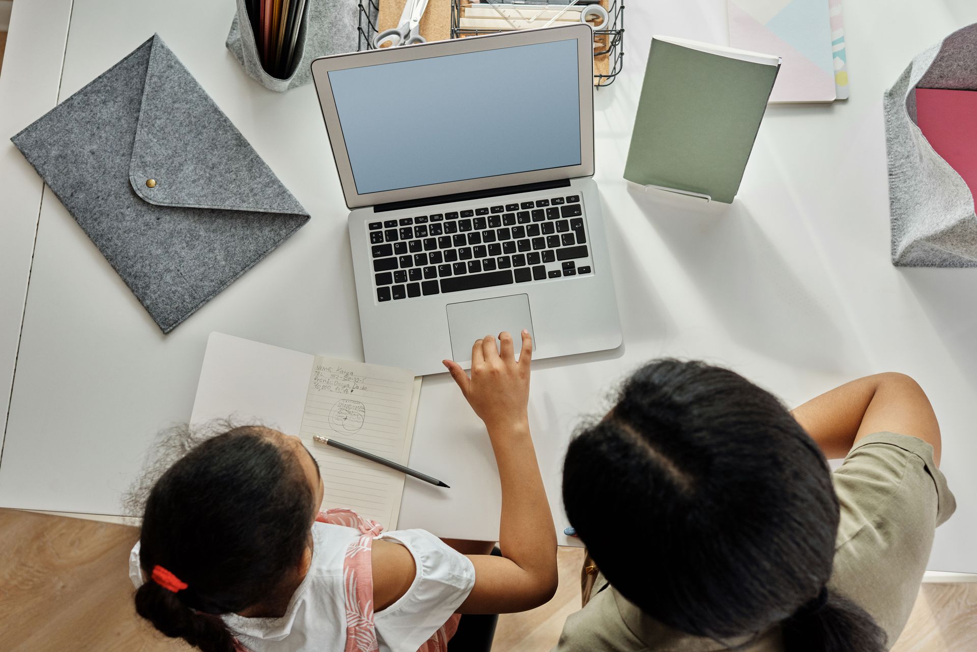 Two people working at a desk with a laptop, notebooks, and papers in a bright office overhead view