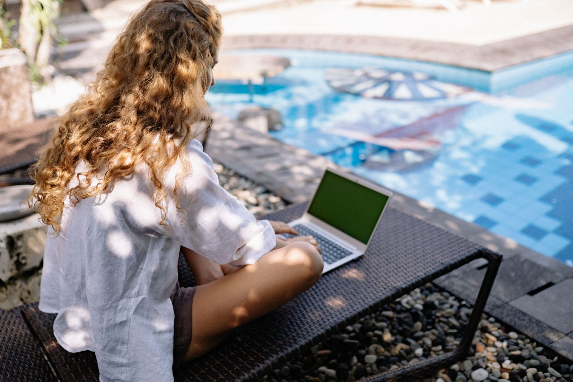 Person using a laptop outdoors beside a pool