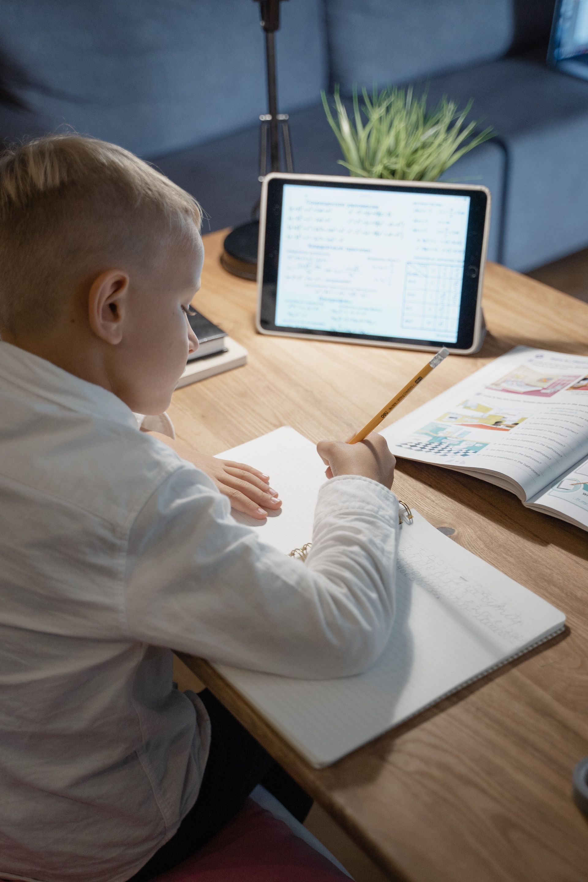 Person studying at a wooden desk with a tablet and open notebook in a home office.