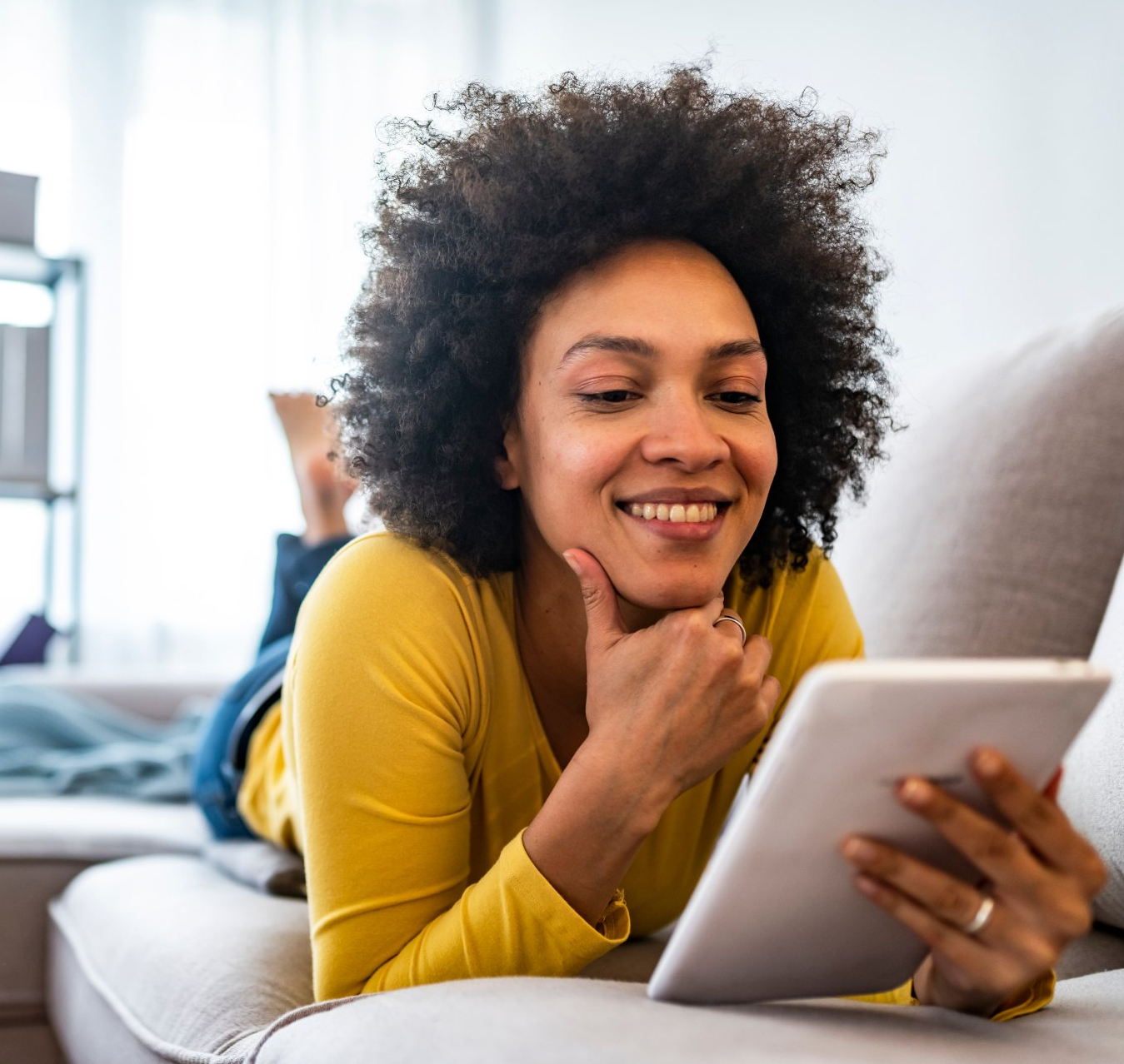 A woman is laying on a couch using a tablet computer.