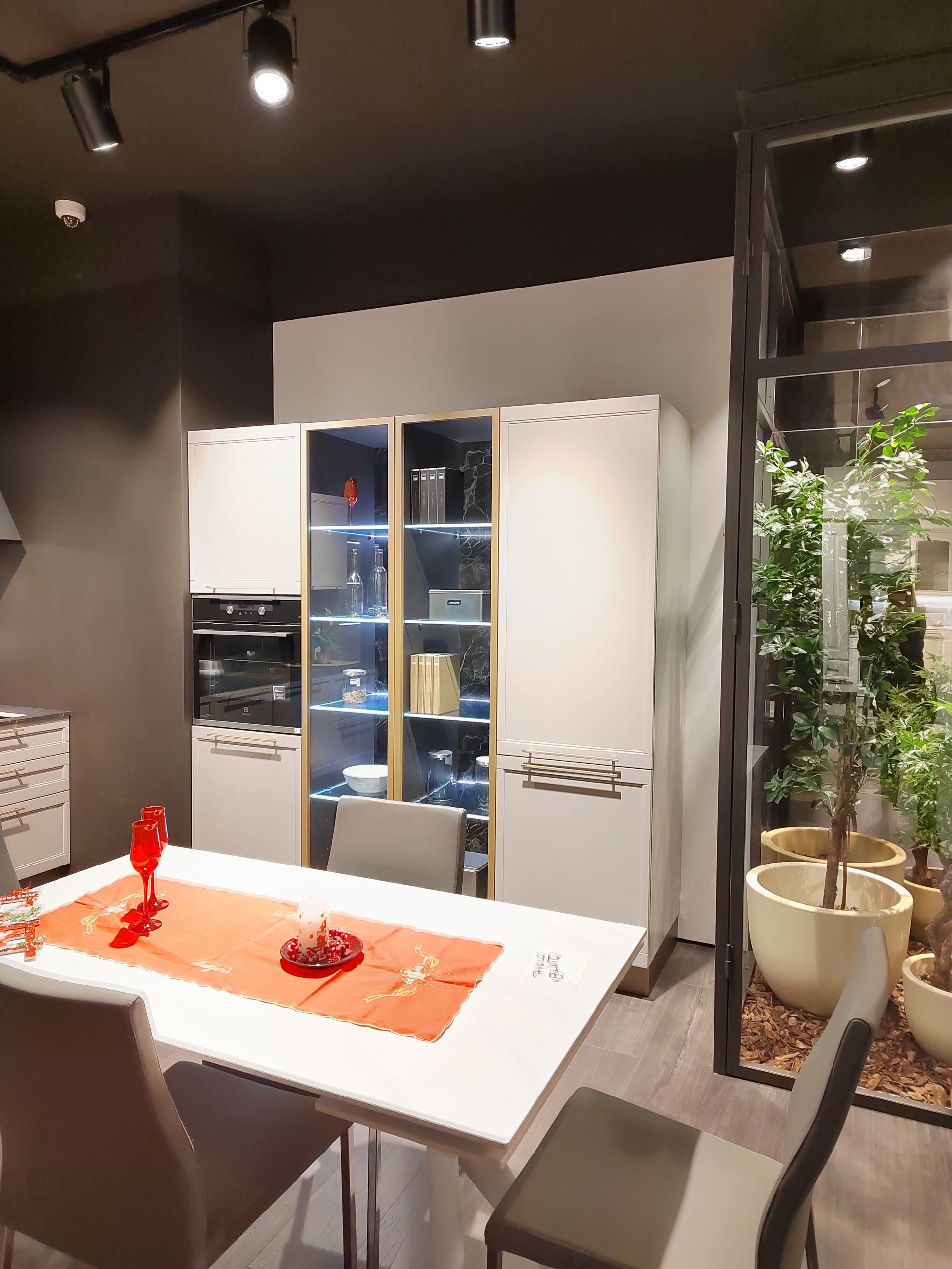 Cucina moderna con mobili bianchi, tavolo apparecchiato per la cena e giardino con pareti in vetro.