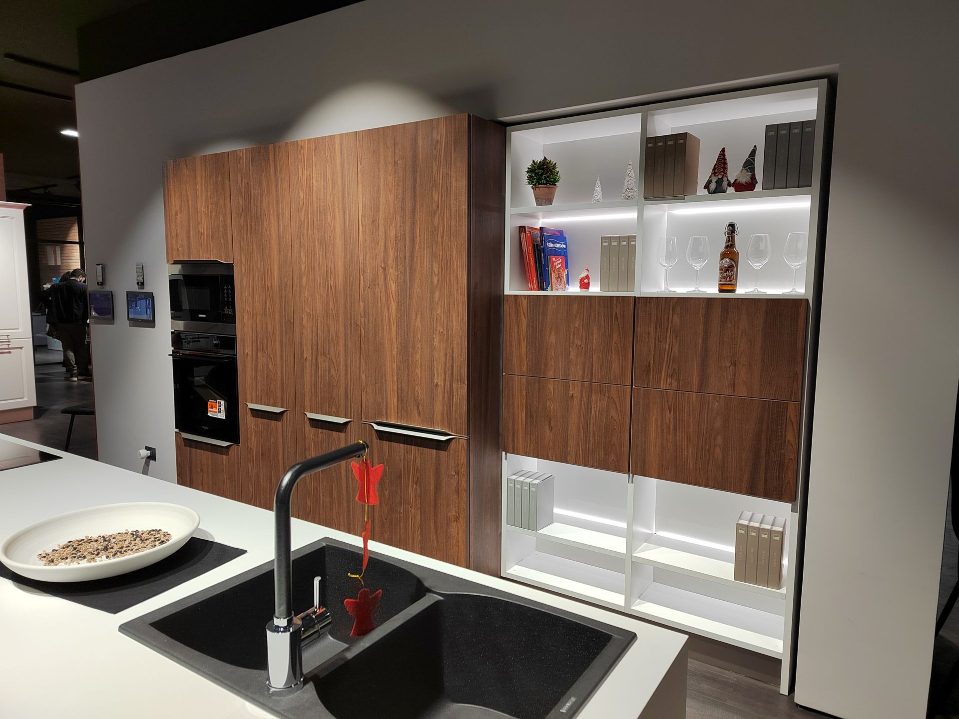 Cucina moderna con mobili in legno scuro, elettrodomestici da incasso e doppio lavello. Mensole illuminate.