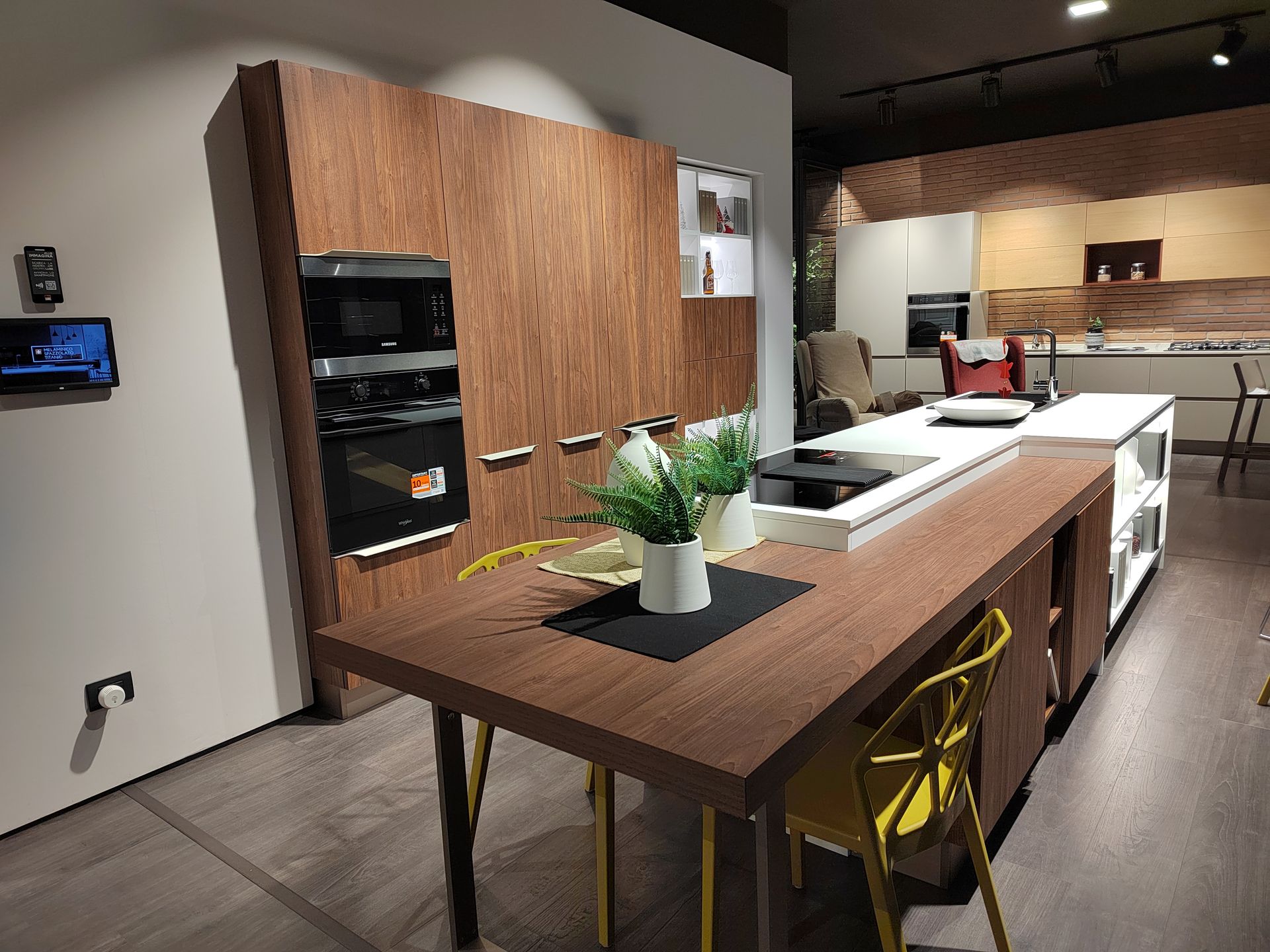 Cucina moderna con mobili in legno, isola con piano cottura e tavolo da pranzo con sedie gialle.