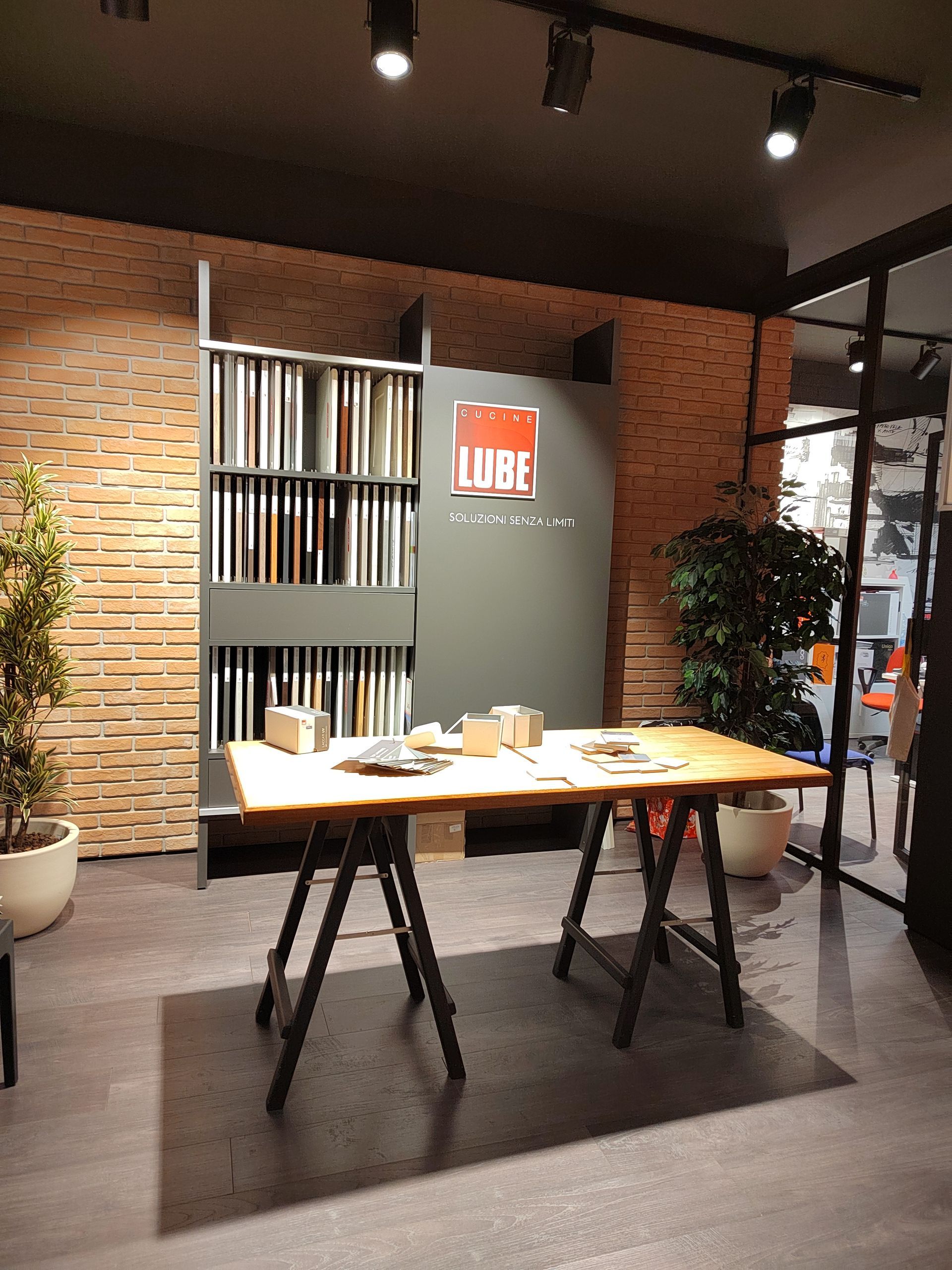 Showroom interno con tavolo in legno, esposizione di campioni e parete in mattoni.