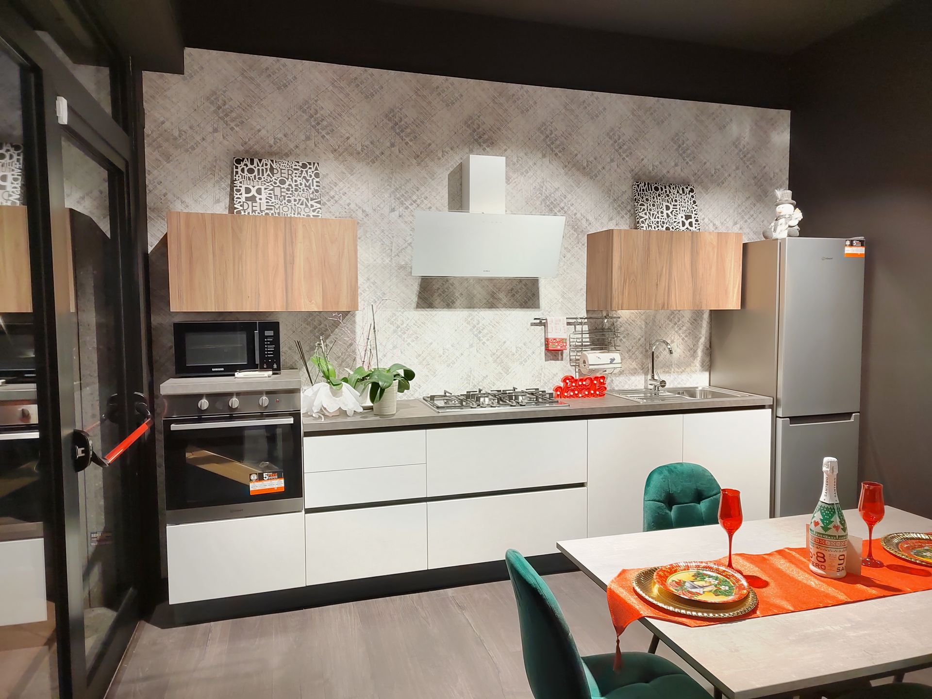 Cucina moderna con mobili bianchi, dettagli in legno e tavolo da pranzo apparecchiato con stoviglie.