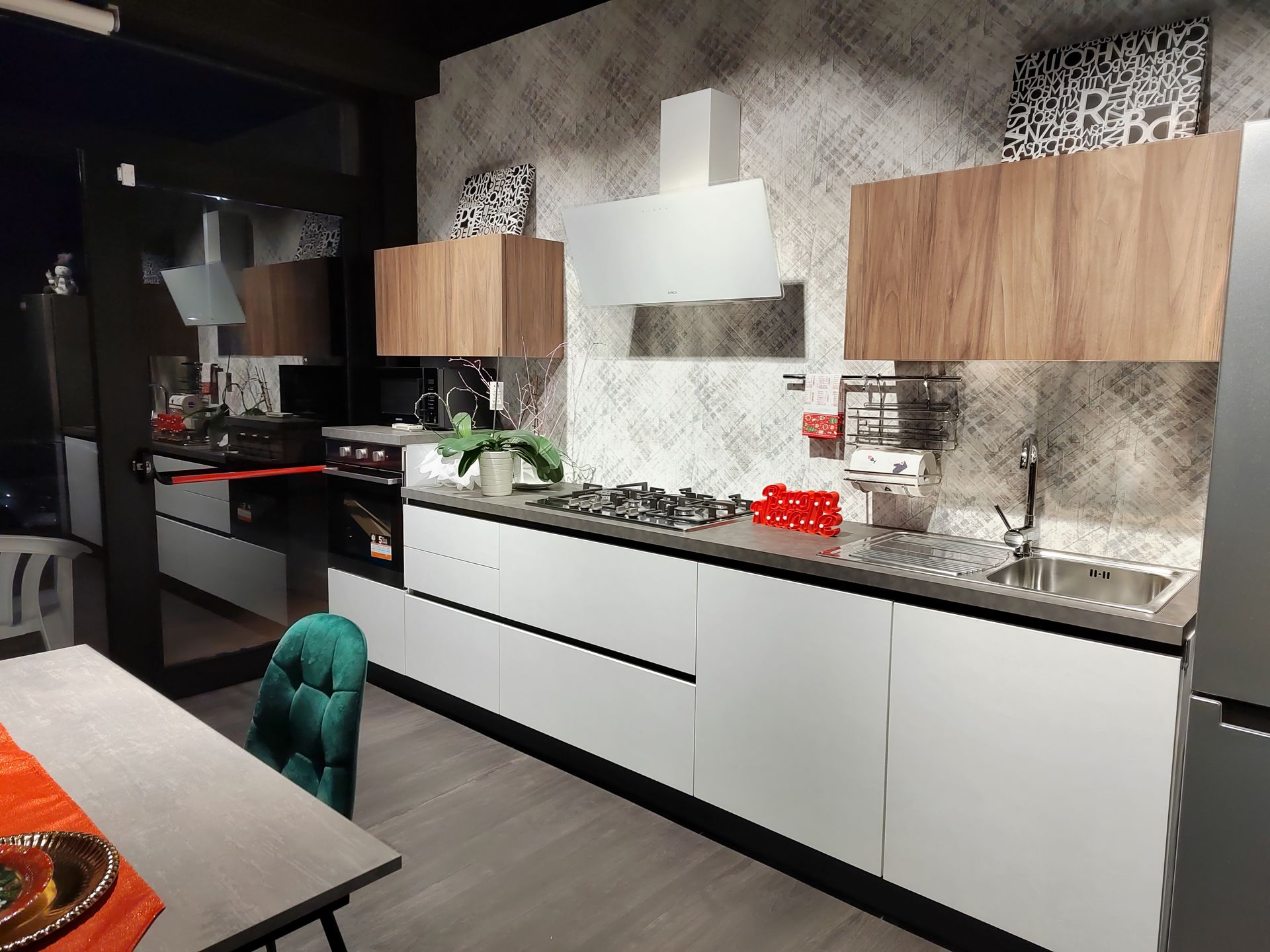 Cucina moderna con mobili bianchi, dettagli in legno e ripiani grigi.