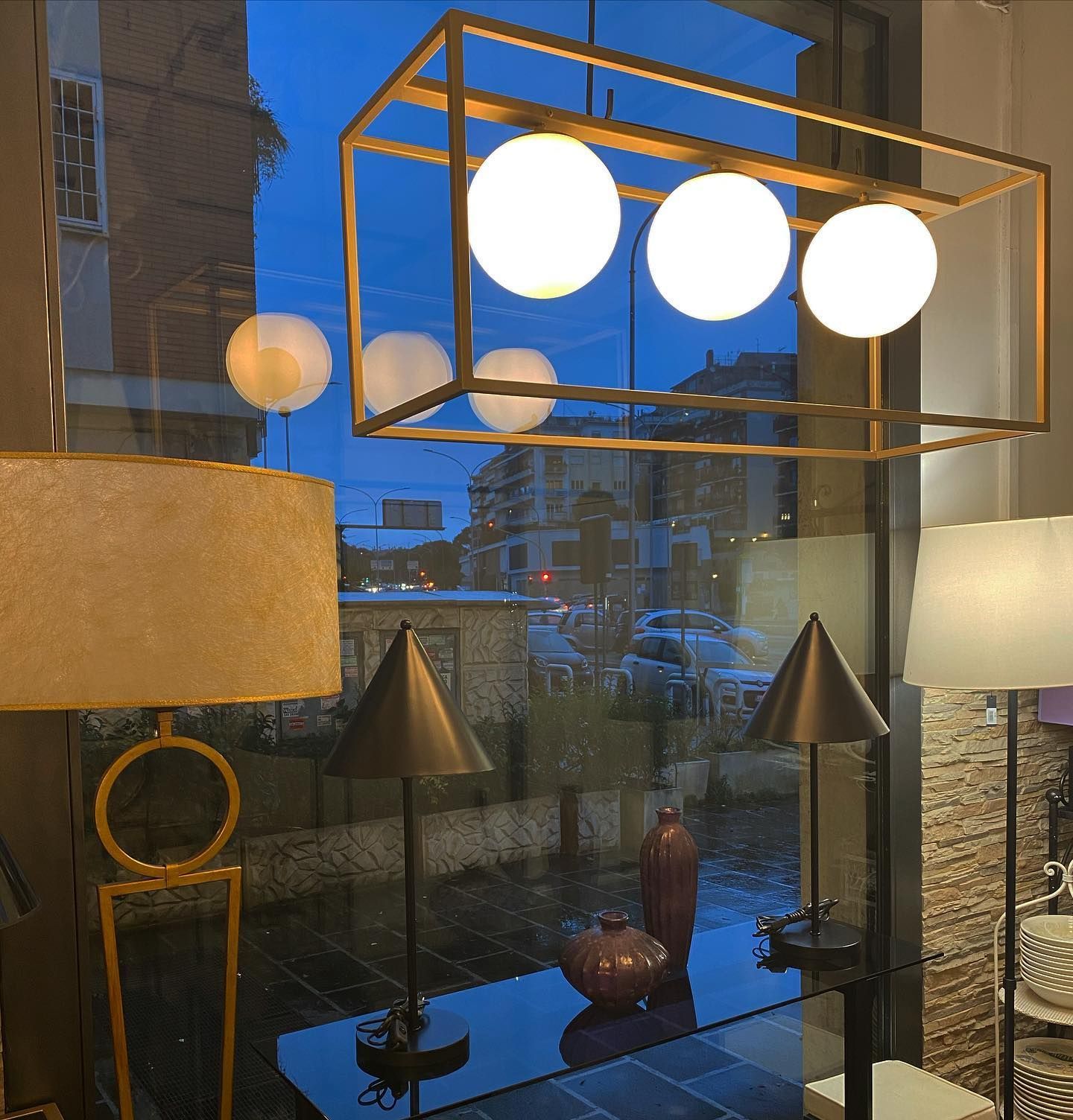 Vetrina con lampade decorative, globi bianchi luminosi e una strada cittadina riflessa nel vetro.