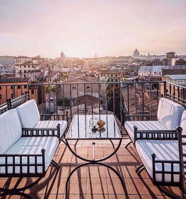 Terrazza sul tetto con sedie e tavolo bianchi con vista sullo skyline della città al tramonto.