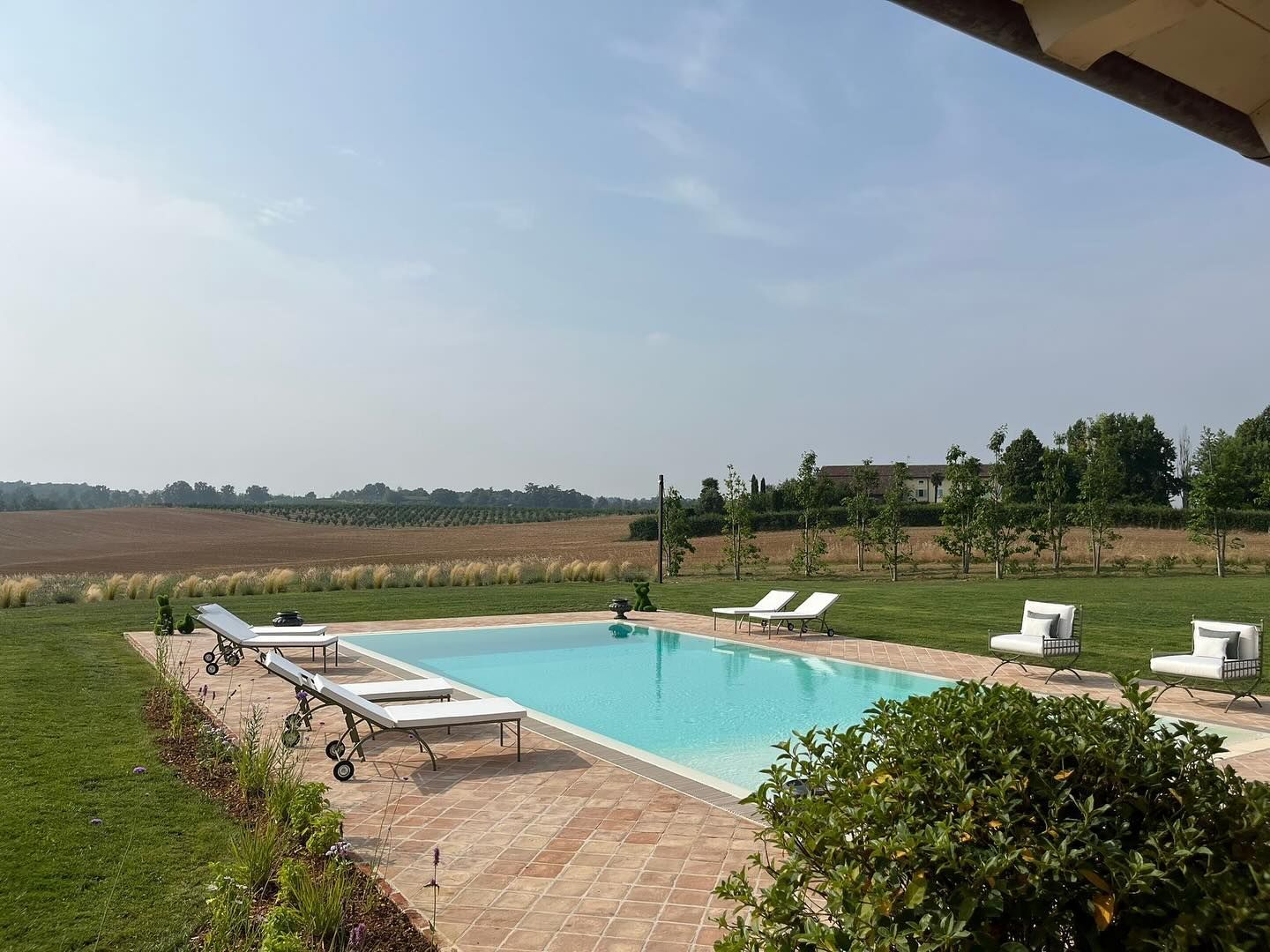 Piscina all'aperto con lettini prendisole accanto a un paesaggio erboso e aperto sotto un cielo limpido.