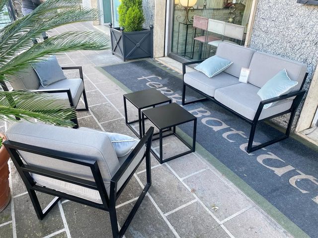 Patio esterno con sedute grigie, tavolino da caffè nero e piante in vaso su una terrazza in pietra.