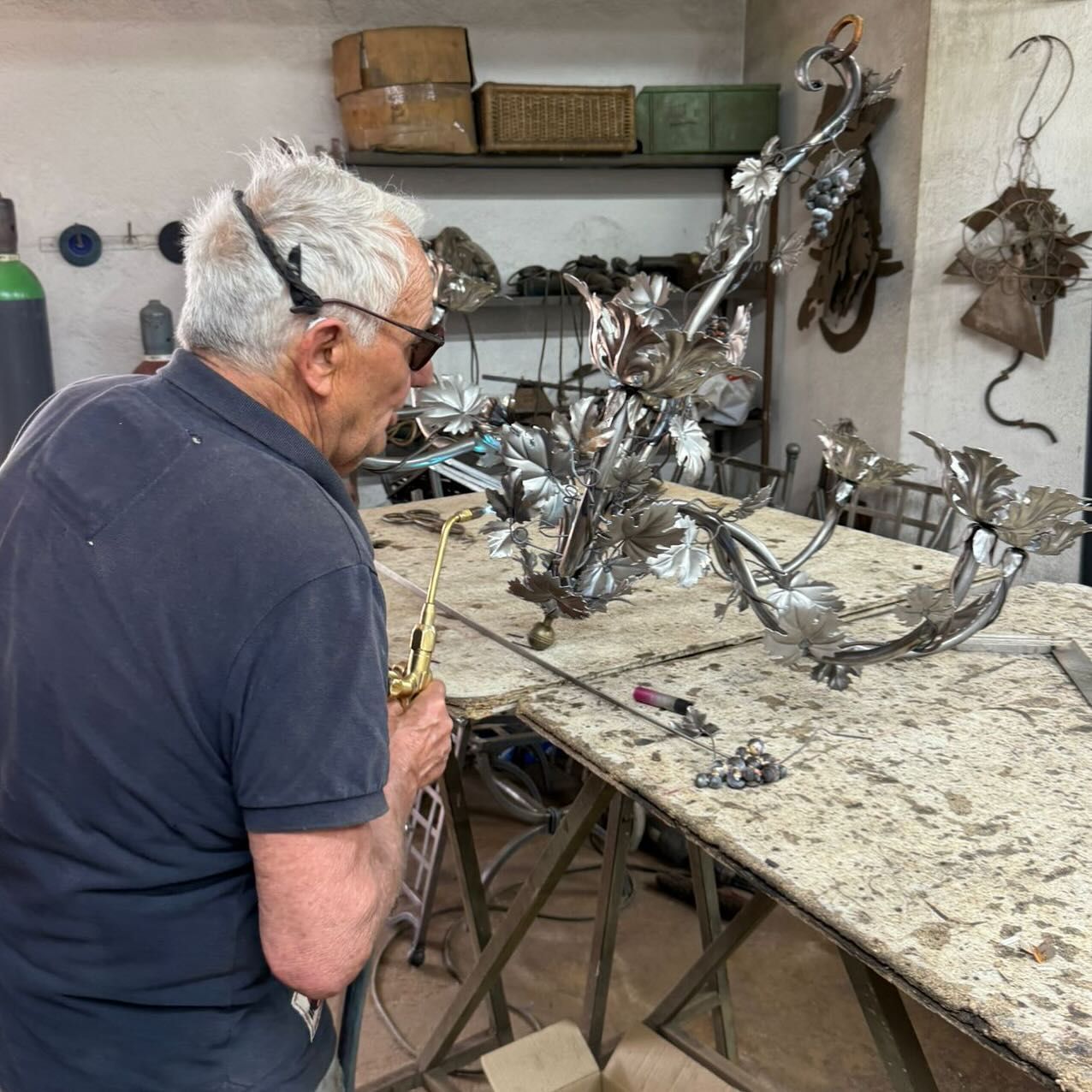 Un uomo in un'officina ispeziona delle sculture in metallo su un tavolo da lavoro.
