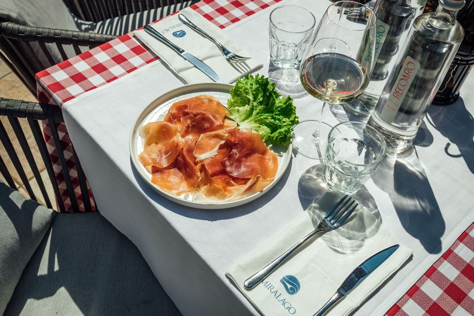 Dolce rosso a forma di cuore su un piatto beige, guarnito con salsa rossa e cioccolato fondente, su una tovaglia blu.