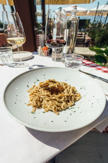 Tonno affettato e scottato su rucola e pomodori secchi, condito con olio, servito su un piatto bianco.