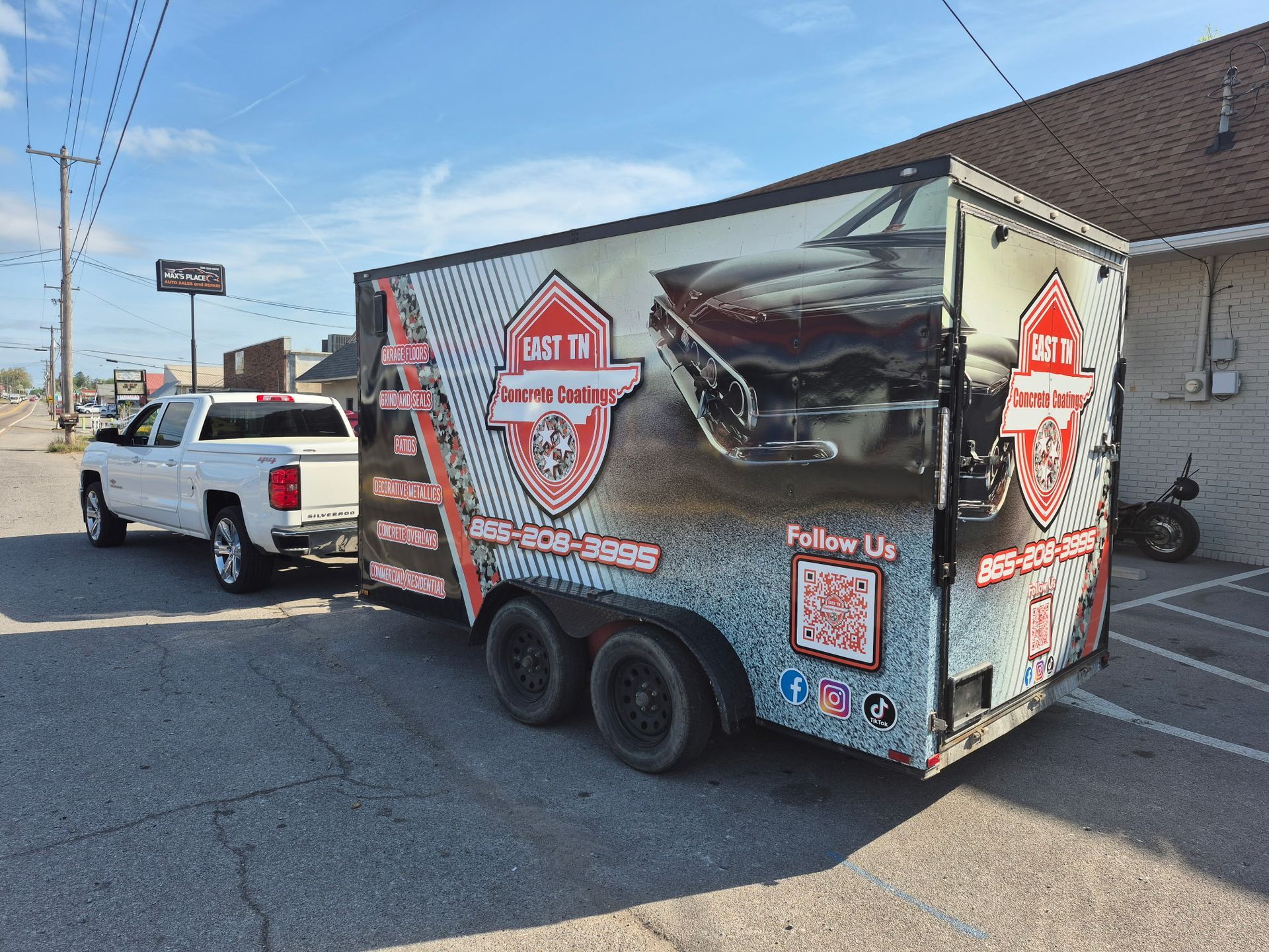 Black business trailer with red decals parked beside a white pickup in a lot.