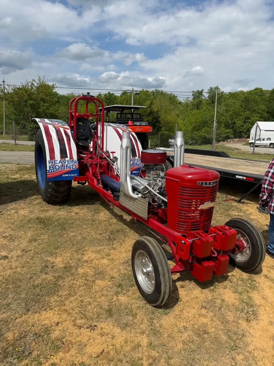 Vintage red tractor with patriotic red, white, and blue decor parked outdoors on grass under cloudy sky
