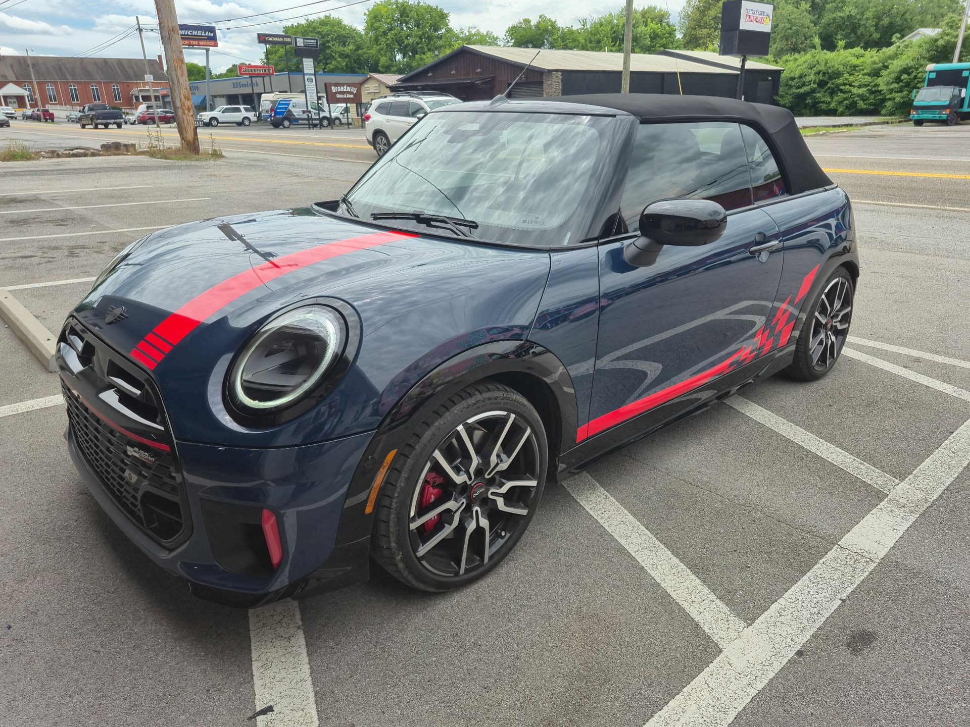 Dark blue Mini Cooper convertible with red racing stripes parked in a lot