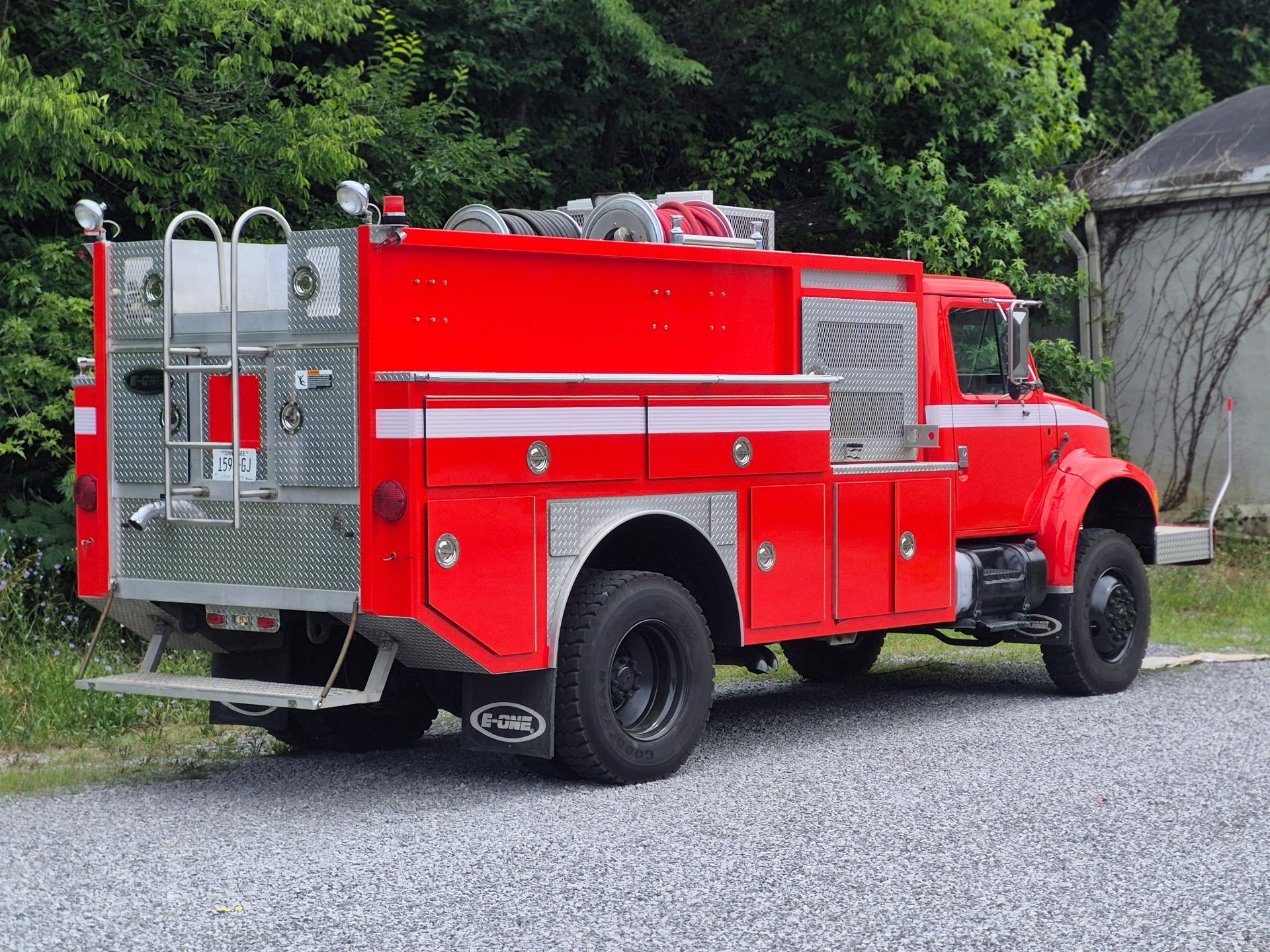 Red fire truck parked on gravel near trees and a building