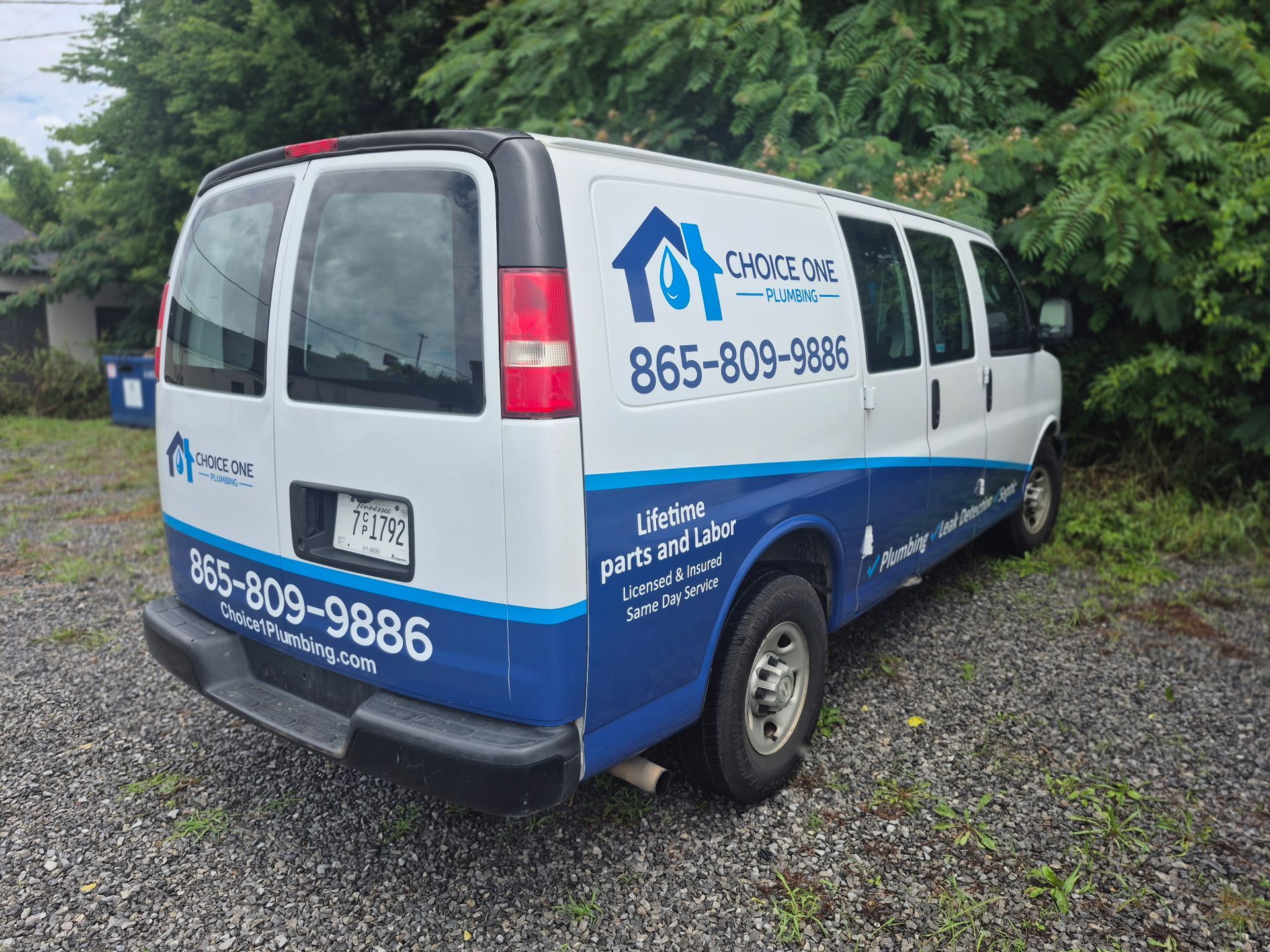 White and blue service van with company branding parked on gravel near trees